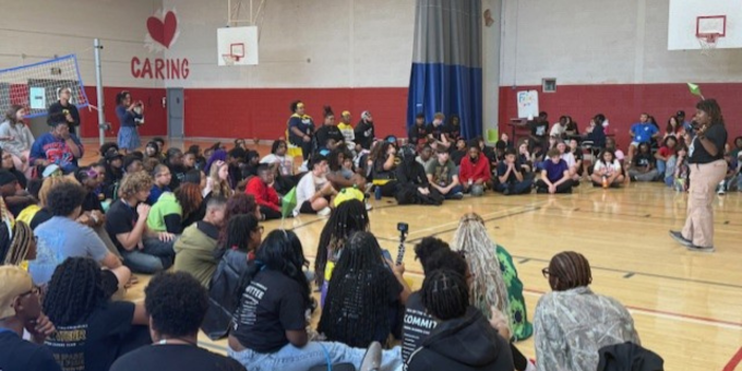 group of teens sitting on a gym floor at a rally