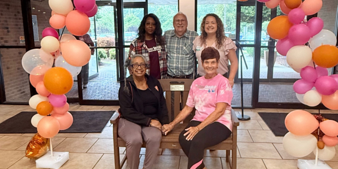 group of women sitting on a bench with balloons behind them