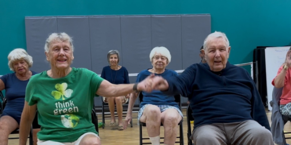 two seniors sitting in chairs doing group exercise in a gym