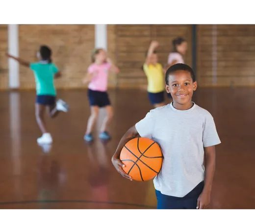 boy with basketball with kids playing in the background
